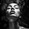 Fantasy art poster. The Woman Underwater Black and White 1 features a woman with closed eyes and parted lips submerged underwater, air bubbles rising around her face, and her hair flowing upwards in dramatic black-and-white lighting.