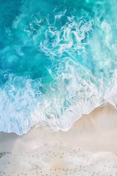 Aerial view of turquoise ocean waves washing onto a sandy beach, with white sea foam and small bird footprints visible on the sand. Beachscape art print available in A1 to A4 sizes.