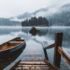 A wooden dock and canoe sit on a calm lake with misty mountains and dense trees in the background. Nature and landscape print available in A1 to A4 sizes.