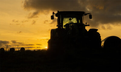 A tractor is silhouetted against a sundown sky with clouds, standing in a field with some grass and fencing visible in the foreground. Nature and landscape poster available in A1 to A4 sizes.