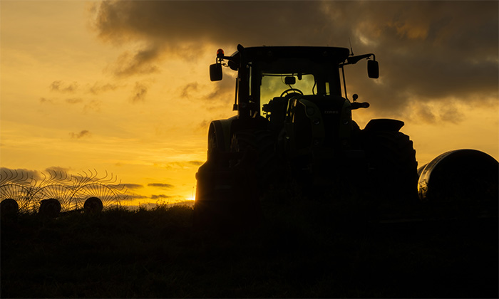 product-image-7-4 A tractor is silhouetted against a sundown sky with clouds, standing in a field with some grass and fencing visible in the foreground. Nature and landscape poster available in A1 to A4 sizes.