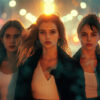 Three young women stand side by side at night, illuminated by bright city lights and blurred traffic in the background. Cinematic-style teen attitude poster available in A1 to A4 sizes.