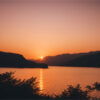 product-image-3-2 Sunset over a calm lake with silhouetted mountains in the background and shrubbery in the foreground. Nature and landscape print available in A1 to A4 sizes.