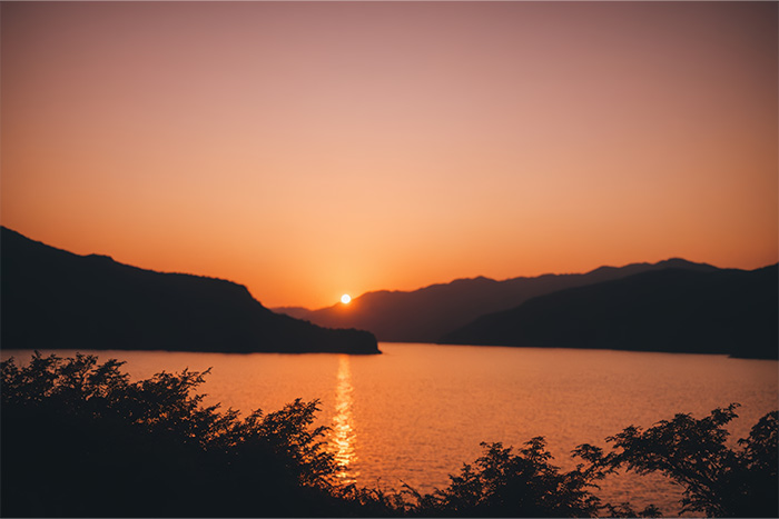 product-image-3-2 Sunset over a calm lake with silhouetted mountains in the background and shrubbery in the foreground. Nature and landscape print available in A1 to A4 sizes.