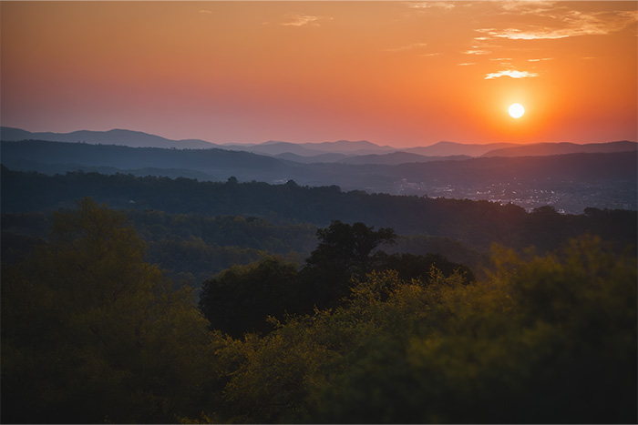product-image-3-2 A sunset over rolling hills with the sun low in the sky, casting an orange glow over the landscape and silhouetted trees in the foreground. Nature and landscape print available in A1 to A4 sizes.