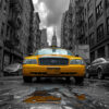 A yellow taxi is parked on a wet city street, surrounded by tall, monochrome buildings under a cloudy sky. New York taxi print available in A1 to A4 sizes.