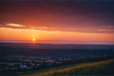 Sunset over a rural landscape with fields, a small village, and distant mountains under a partly cloudy sky. Nature and landscape print available in A1 to A4 sizes.