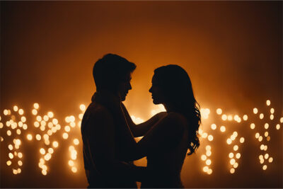 Silhouette of a couple facing each other and embracing, with warm, out-of-focus lights in the background. Romantic wall art print available in A1 to A4 sizes.
