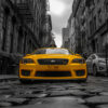 Yellow taxi cab centred on a cobblestone street in a city, with tall buildings and a cloudy sky in black and white in the background. New York taxi print available in A1 to A4 sizes.
