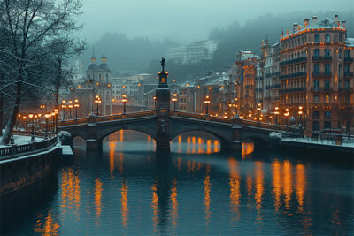 A stone bridge spans a river in a city at dusk, with snow on the ground and warm streetlights reflecting in the water. Historic buildings line the riverbanks. Wall art print available in A1 to A4 sizes.
