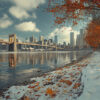 View of a city skyline and bridge across a river, with autumn trees and fallen leaves alongside snow on the ground under a partly cloudy sky. Wall art print available in A1 to A4 sizes.