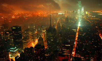 Aerial view of a city skyline at night with illuminated buildings, dense fog, and glowing lights, under a cloudy, orange-tinted sky. Wall art print available in A1 to A4 sizes.