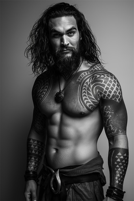product-image-2-3 An art portrait of Jason Momoa, with long hair, a beard, and tribal tattoos on his arms and chest stands shirtless, wearing a necklace and wristbands, against a plain background. Wall art print available in A1 to A4 sizes.