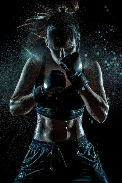A female boxer wearing black gloves and sportswear stands in a fighting stance, with sweat and water droplets visible against a dark background. Poster print available in A1 to A4 sizes.
