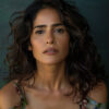 Portrait of Salma Hayek, with wavy dark hair, wearing a floral off-shoulder top as she looks directly at the camera against a dark green background. Wall art print available in A1 to A4 sizes.