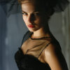 Natalie Portman poses under dramatic lighting in a black mesh dress and veil, looking toward the camera with a neutral expression in this striking portrait. Wall art print available in A1 to A4 sizes.
