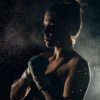 A female boxer in sportswear and gloves stands in a fighting stance, illuminated from behind with water droplets suspended in the air. Poster print available in A1 to A4 sizes.