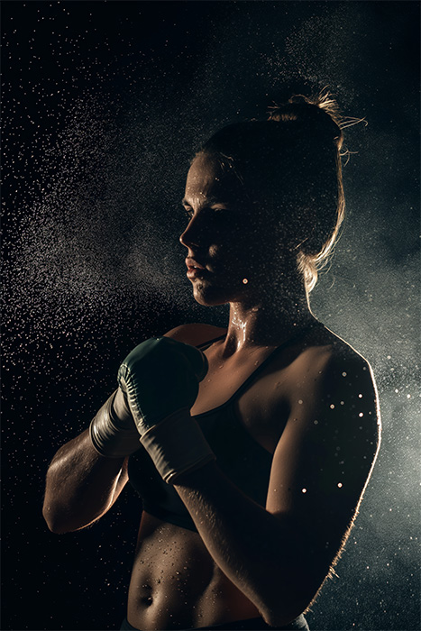 product-image-2-3 A female boxer in sportswear and gloves stands in a fighting stance, illuminated from behind with water droplets suspended in the air. Poster print available in A1 to A4 sizes.