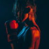 A woman in sportswear and boxing gloves stands in a boxing pose, lit by dramatic red and blue lighting against a dark background. Poster print available in A1 to A4 sizes.