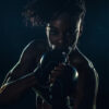 A woman wearing boxing gloves poses in a fighting stance against a dark background, illuminated by dramatic lighting. Poster print available in A1 to A4 sizes.
