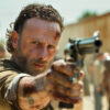 A bearded man with a dirty face, resembling Rick Grimes from The Walking Dead, points a revolver towards the camera outdoors, with blurred people and buildings in the background. Horror poster available in A1 to A4 sizes.