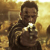 A man with a dirty face, resembling Rick Grimes from The Walking Dead, points a handgun toward the camera as several zombie-like figures approach in a blurred, sunlit background. Horror poster available in A1 to A4 sizes.