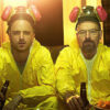 Two men in yellow hazmat suits and respirators sit on a couch, holding beer bottles with a tray of snacks before them, illuminated by warm indoor lighting—a scene from Breaking Bad. Poster print available in A1 to A4 sizes.