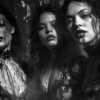 Three women in black lace outfits stand close together, with dark liquid resembling ink or blood streaming from their eyes and mouths, set against a smoky, dimly lit background. Fantasy art poster available in A1 to A4 sizes.