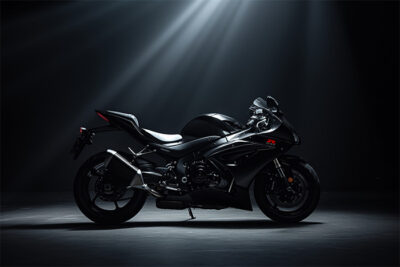 A sleek black Suzuki GSXR-1000 sport motorcycle is displayed in a dark studio, illuminated by overhead spotlights highlighting its aerodynamic design. Wall art print available in A1 to A4 sizes.