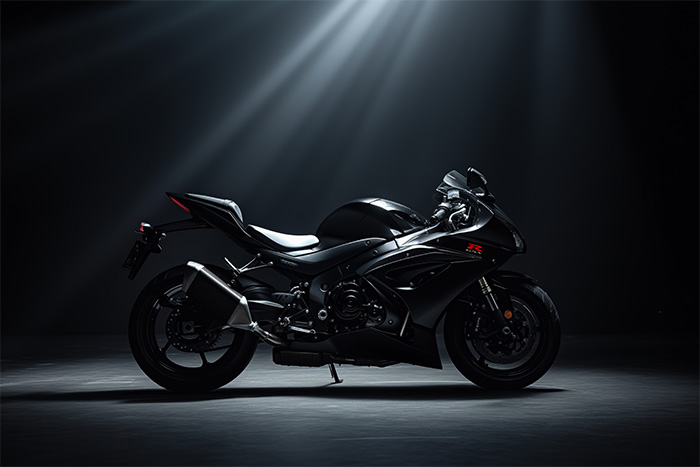 product-image-3-2 A sleek black Suzuki GSXR-1000 sport motorcycle is displayed in a dark studio, illuminated by overhead spotlights highlighting its aerodynamic design. Wall art print available in A1 to A4 sizes.