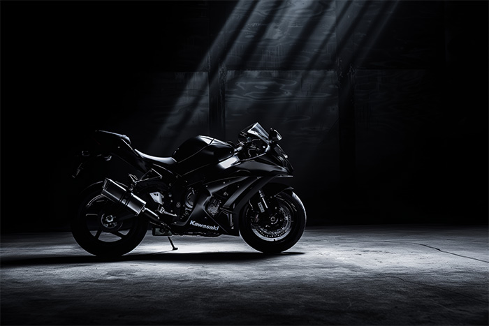 product-image-3-2 A black Kawasaki ZX10R sport motorcycle is parked on a dimly lit concrete floor with beams of light shining down from above. Wall art print available in A1 to A4 sizes.
