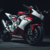A red and white Honda CBR1000RR sport motorcycle is parked indoors on a concrete floor, with dim lighting highlighting its sleek design and striking details. Wall art print available in A1 to A4 sizes.