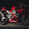 A red Honda CBR1000RR sport motorcycle is parked on a dark surface, illuminated by focused lighting that highlights its sleek design and branding. Wall art print available in A1 to A4 sizes.