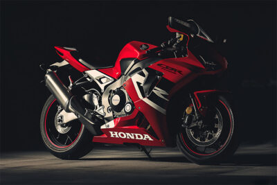 A red Honda CBR1000RR sport motorcycle is parked on a dark surface, illuminated by focused lighting that highlights its sleek design and branding. Wall art print available in A1 to A4 sizes.