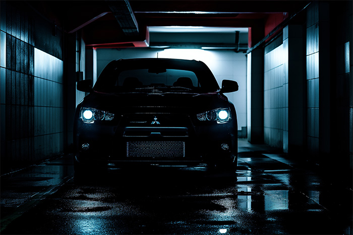 A black Mitsubishi Evo 3 with headlights on is parked in a dimly lit, reflective underground garage. Wall art print available in A1 to A4 sizes.