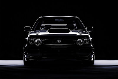 Front view of a black Subaru Impreza with prominent headlights and hood scoop, set against a dark background with dramatic lighting. Wall art print available in A1 to A4 sizes.