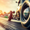 Close-up of a vintage car tire on a race track at sunset, with sunlight reflecting off the chrome hubcap and blurred background. Wall art print available in A1 to A4 sizes.