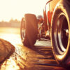 Close-up view of a race cars rear wheel on a racetrack at sunset, with sunlight reflecting off the car and tire marks visible on the track surface. Wall art print available in A1 to A4 sizes.