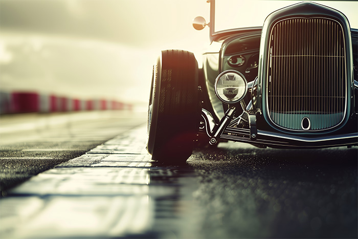 product-image-3-2 A vintage car with exposed front wheels is parked on a wet racetrack, with the sun shining in the background. Wall art print available in A1 to A4 sizes.