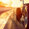 Close-up of a vintage car parked on a racetrack at sunset, with sunlight casting long shadows and highlighting the cars tire and body. Wall art print available in A1 to A4 sizes.