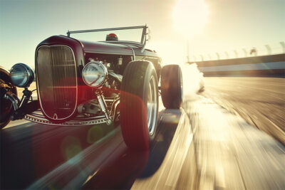 A vintage hot rod car speeds down a sunlit racetrack, with smoke trailing from its tires and blurred motion in the background. Wall art print available in A1 to A4 sizes.