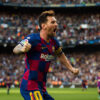 Soccer player Lionel Messi in a blue and red Barcelona jersey celebrates with clenched fists on the field, with a crowd of spectators cheering in the background. Poster print available in A1 to A4 sizes.