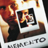 A close-up Polaroid photo of a serious man from the 2000 movie Memento, with a smaller photo of a woman inside it, and the word MEMENTO handwritten at the bottom. Movie poster print available in A1 to A4 sizes.