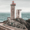 A stone Lighthouse and adjacent building stand on rocky cliffs by the sea, with choppy water and a cloudy sky in the background. Nature and landscape poster print available in A1 to A4 sizes.