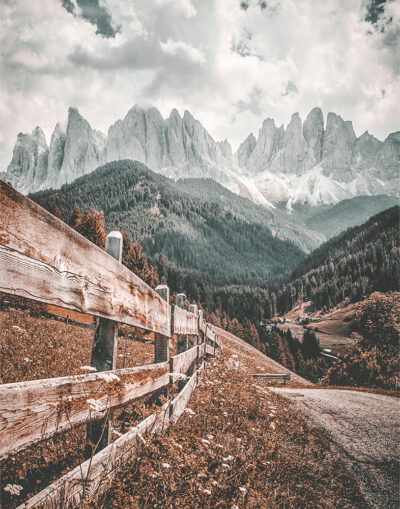 A wooden fence lines a grassy hill with a winding mountain path, forested slopes, and jagged mountains in the background under a cloudy sky. Nature and landscape poster print available in A1 to A4 sizes.