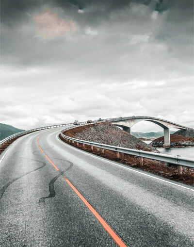 Curved road leading to an arched bridge under a cloudy sky, with metal guardrails on both sides and distant hills visible. Nature and landscape poster print available in A1 to A4 sizes.