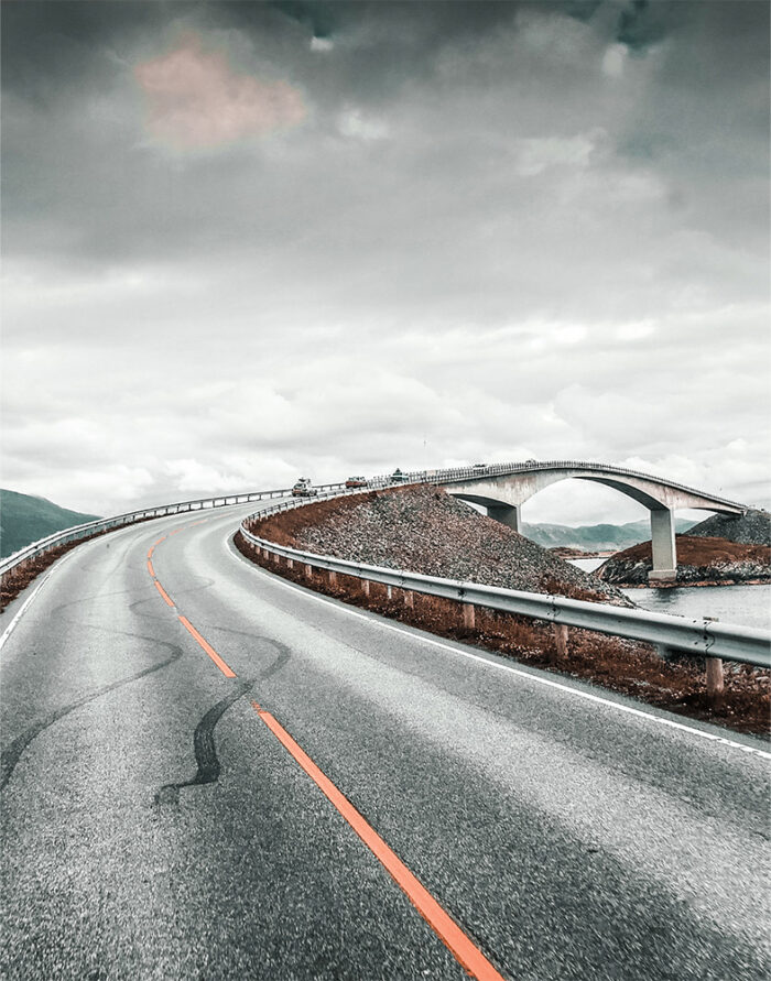 product-image-11-14 Curved road leading to an arched bridge under a cloudy sky, with metal guardrails on both sides and distant hills visible. Nature and landscape poster print available in A1 to A4 sizes.