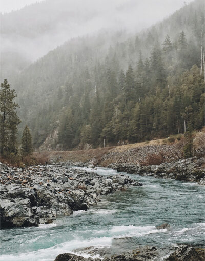 A mountain river flows over rocks through a forested, misty landscape, with pine trees and fog veiling the background. Nature and landscape poster print available in A1 to A4 sizes.