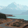 A winding Mountain Road leads toward a large, snow-covered mountain beside a serene lake, with sparse trees and dry grass in the foreground. Nature and landscape poster print available in A1 to A4 sizes.