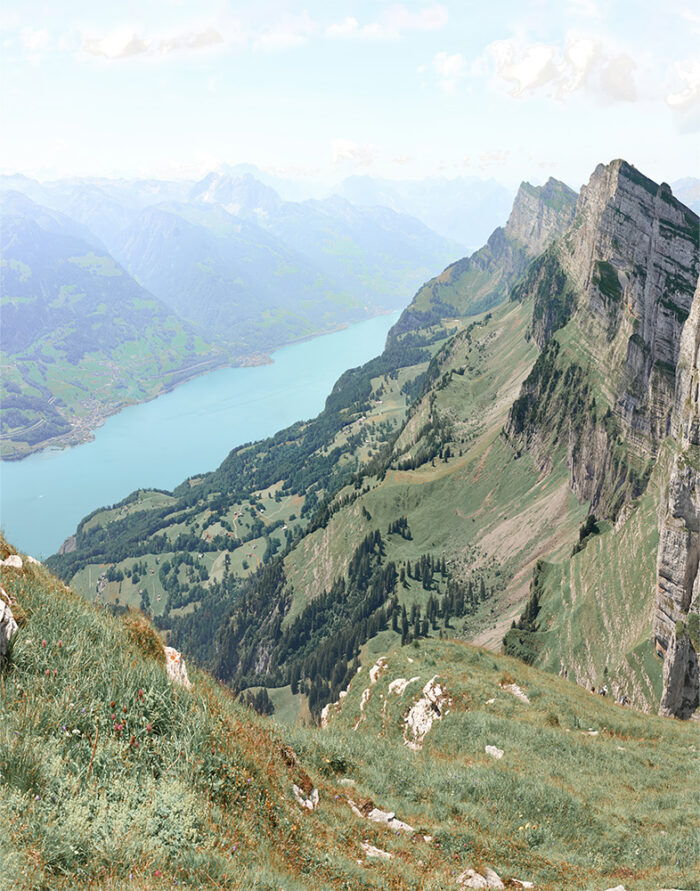 A scenic Mountain View of a turquoise lake bordered by green hills and rocky mountains under a partly cloudy sky. Nature and landscape poster print available in A1 to A4 sizes.